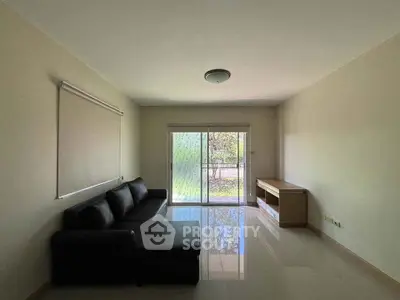 Spacious living room with modern sofa and large window offering natural light and garden view.