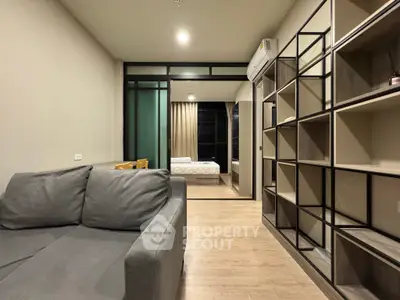 Modern apartment interior with cozy living room and view into bedroom, featuring stylish shelving and neutral tones.