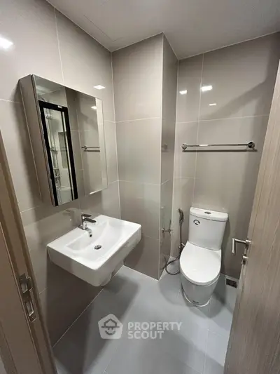 Modern bathroom with sleek fixtures and neutral tiles, featuring a wall-mounted sink and toilet.