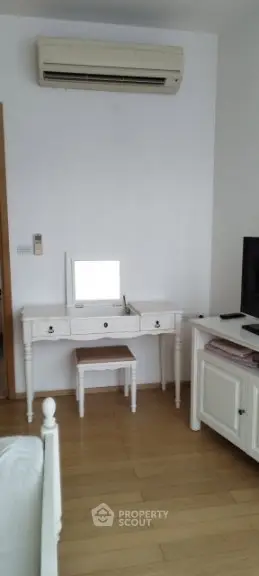 Charming bedroom with elegant white furniture and wooden flooring, featuring a classic vanity and air conditioning.