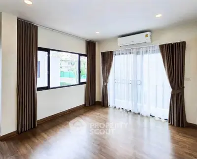 Spacious living room with large windows and elegant curtains, featuring hardwood floors and modern air conditioning.