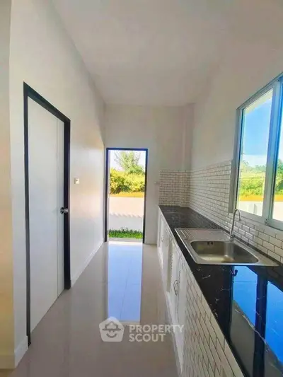 Modern kitchen with sleek design and outdoor view, featuring glossy countertops and white tiled backsplash.
