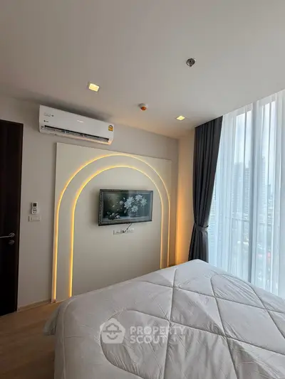 Modern bedroom with stylish lighting and city view, featuring a wall-mounted TV and air conditioning.