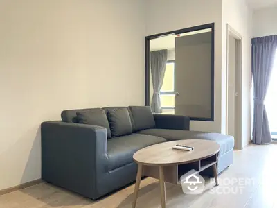 Modern minimalist living room with a comfortable grey sectional sofa, sleek round coffee table, and large mirror creating a spacious feel.