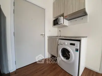 Compact kitchen with washing machine and microwave in modern apartment