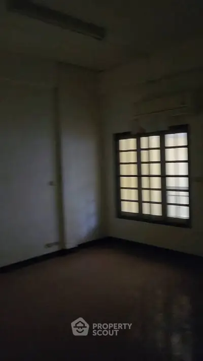 Dimly lit empty room with window and air conditioning unit.