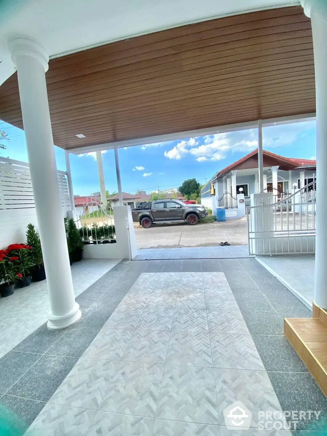 Spacious covered porch with elegant white columns and tiled flooring, offering a welcoming entrance to a beautiful suburban home with a clear blue sky.