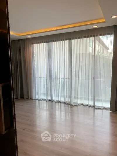 Spacious living room with floor-to-ceiling windows and elegant curtains in modern apartment.