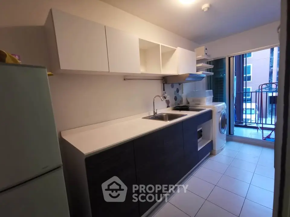 Modern kitchen with sleek cabinetry and appliances, featuring a washing machine and balcony access.