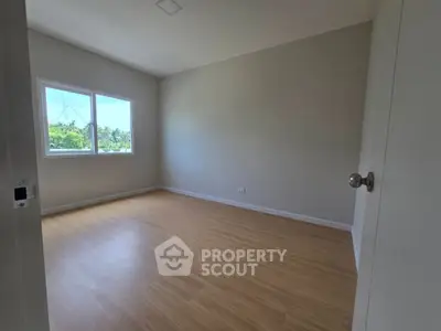Spacious empty bedroom with wooden flooring and large window offering natural light.