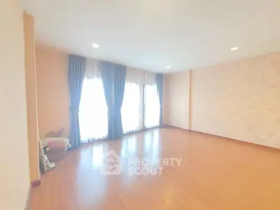 Spacious empty room with wooden flooring and large windows, perfect for customization.