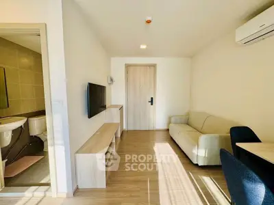 Modern living room with cozy sofa, wall-mounted TV, and adjacent bathroom in a bright apartment.