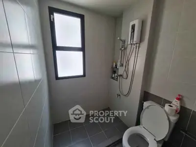Modern bathroom with shower and toilet, featuring sleek tiles and natural light from window.