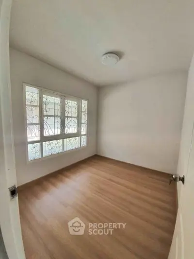 Spacious empty bedroom with large window and wooden flooring, perfect for customization.