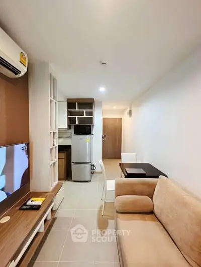 Modern living room with open kitchen, featuring cozy sofa and sleek appliances in a compact layout.