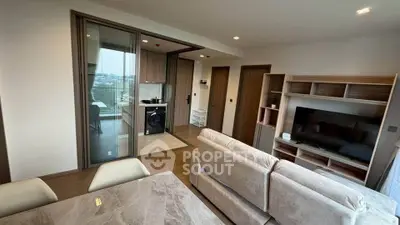 Modern living room with open kitchen and balcony view, featuring sleek furniture and a washing machine.