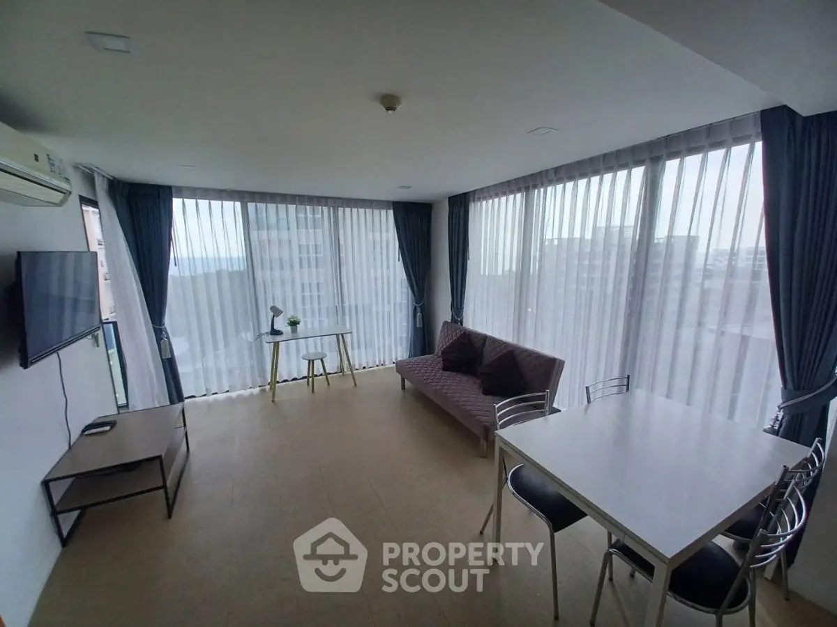 Spacious living room with large windows and modern furnishings in a high-rise apartment.