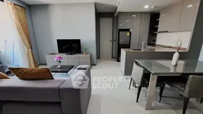 Modern open-layout living room with sleek kitchen and dining area, featuring stylish furniture and neutral tones.