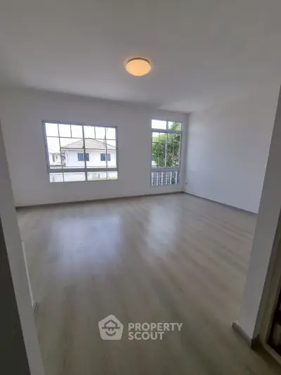 Spacious empty room with large windows and wooden flooring, perfect for customization.