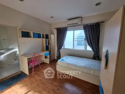 Cozy bedroom with wooden flooring, study desk, and natural light through window.