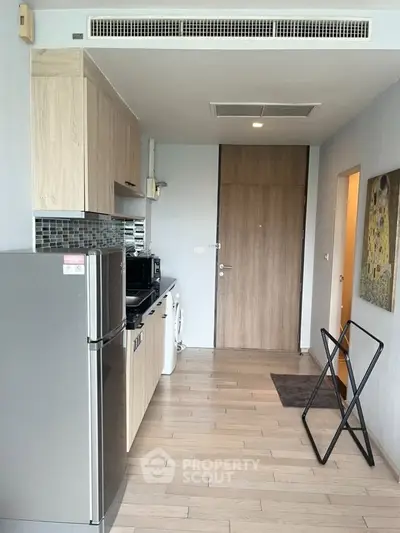 Modern kitchen with wooden cabinets, stainless steel fridge, and washing machine in a compact layout.