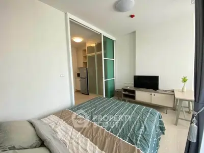 Modern bedroom with sliding glass doors leading to a compact kitchen, featuring a cozy bed and a flat-screen TV.