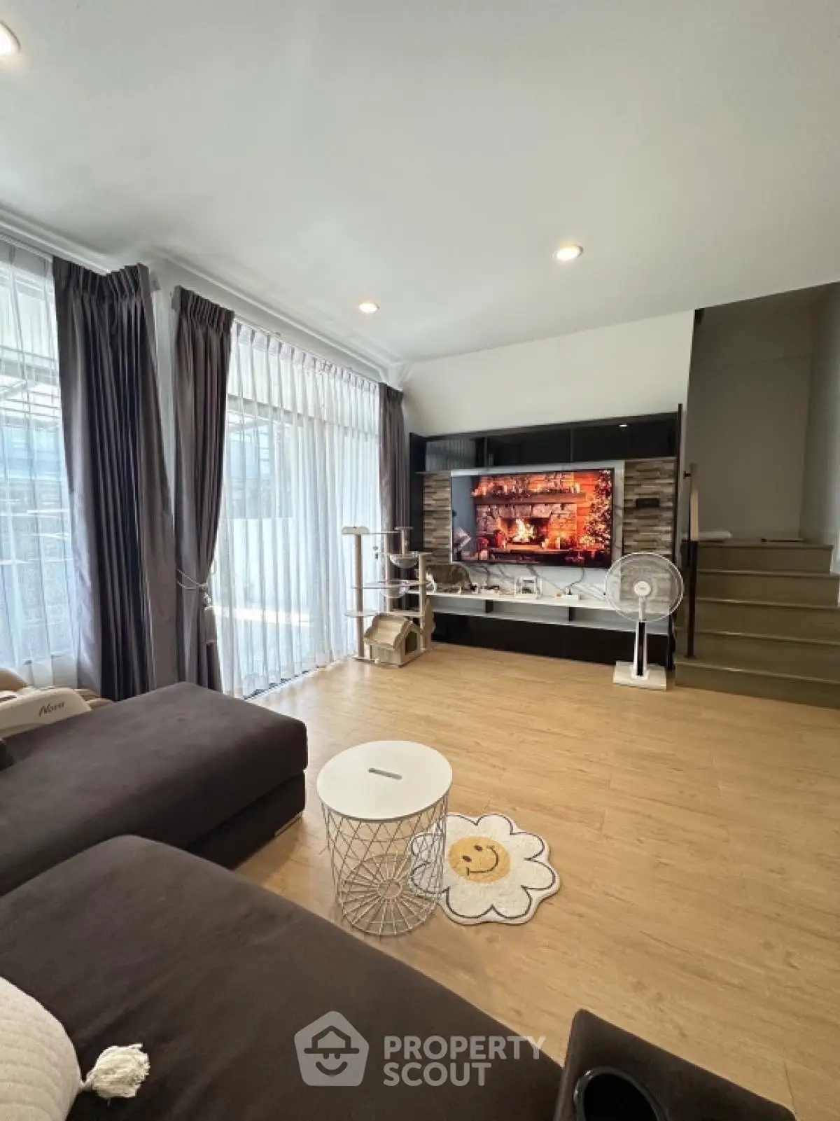 Modern living room with large TV and cozy seating area, featuring stylish decor and natural light.