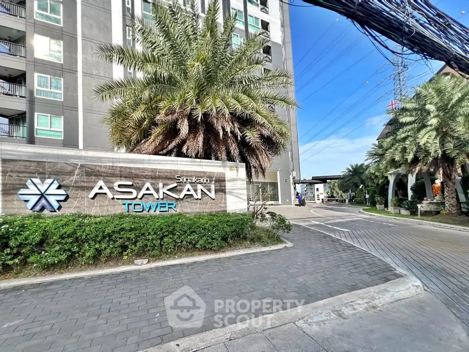 Modern Asakan Tower entrance with lush landscaping and clear blue sky.