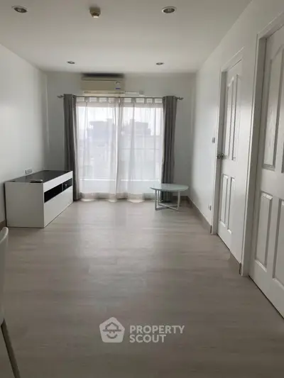 Spacious minimalist living room with large window and modern furnishings.