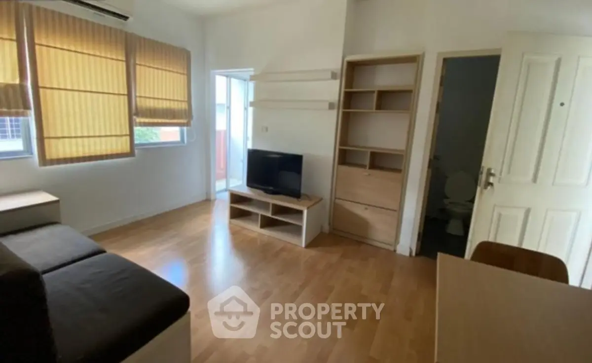 Cozy living room with wooden flooring and natural light, featuring a TV and modern furniture.