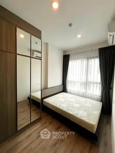 Modern bedroom with wooden flooring, large window, and mirrored wardrobe in a stylish apartment.