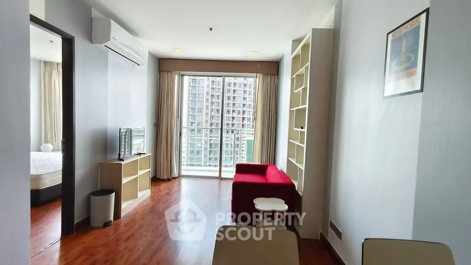 Modern living room with red sofa and large window offering city view in high-rise apartment.