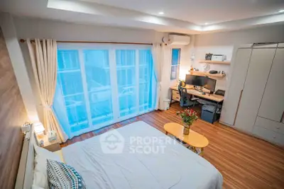 Spacious bedroom with modern decor and work desk, featuring large windows and wooden flooring.