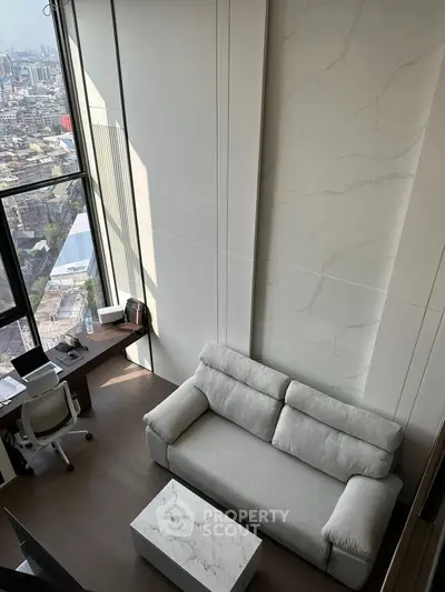 Modern living room with high ceiling and city view, featuring a cozy sofa and workspace.