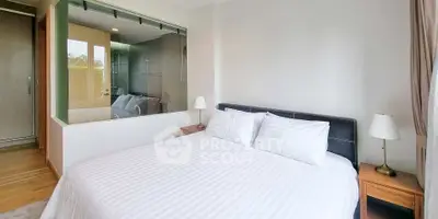 Modern bedroom with large bed and glass wall overlooking bathroom, featuring elegant decor and natural light.