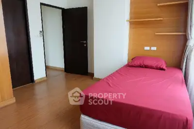 Cozy bedroom with wooden flooring and red bedding, featuring a minimalist design and natural light.