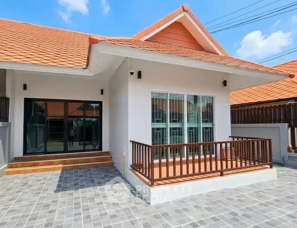 Charming single-story house with red roof and spacious front patio under clear blue sky.