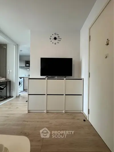 Modern apartment interior with sleek TV stand and wall clock, showcasing open layout and wooden flooring.