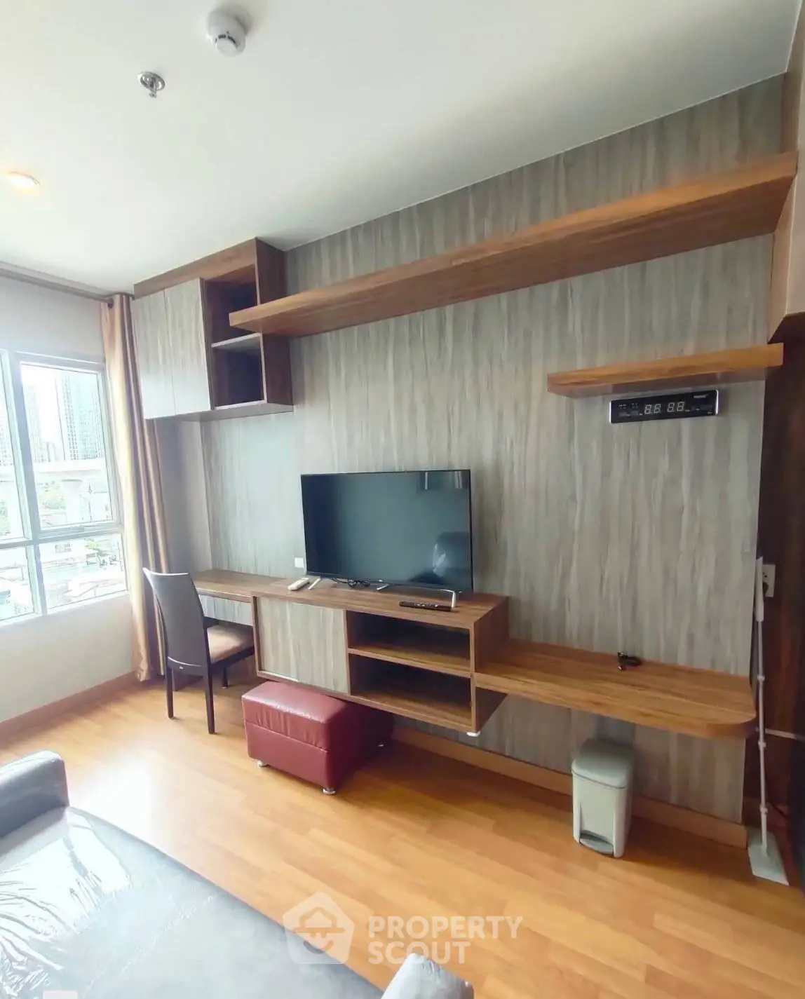 Modern living room with stylish wooden shelves and TV, featuring a city view from the window.