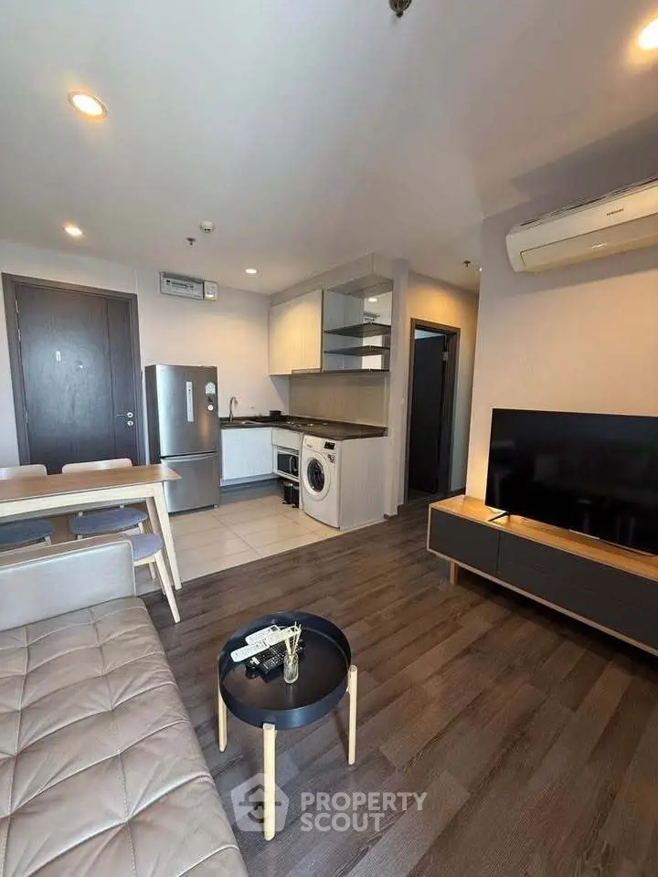 Modern living room with open kitchen, featuring sleek furniture and appliances.