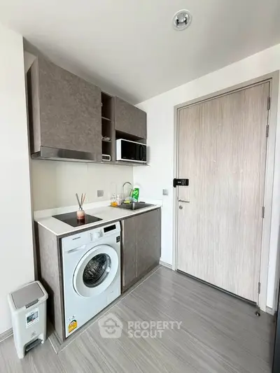Modern compact kitchen with washing machine and microwave in sleek apartment