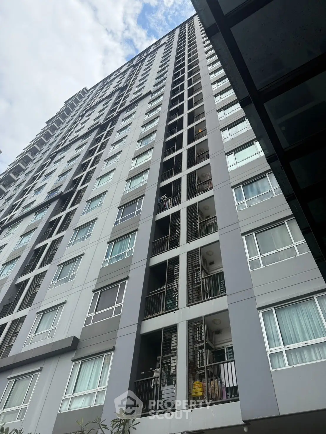 Modern high-rise building with sleek facade and numerous windows under a partly cloudy sky.