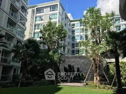 Modern apartment building with lush garden and tall trees, offering serene living environment.