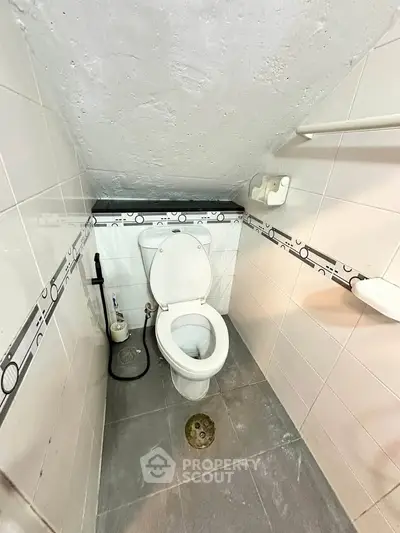 Compact bathroom with white tiles and toilet under sloped ceiling, ideal for small spaces.