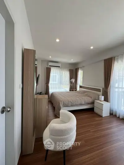 Modern bedroom with cozy decor and natural light, featuring wooden flooring and elegant furnishings.