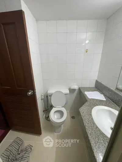 Compact bathroom with tiled walls, modern sink, and toilet in a cozy real estate property.