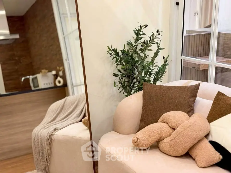 Cozy living room with plush sofa, decorative pillows, and indoor plant, adjacent to a modern kitchen.