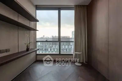 Spacious room with large window offering stunning city view, elegant wooden flooring, and modern shelving.