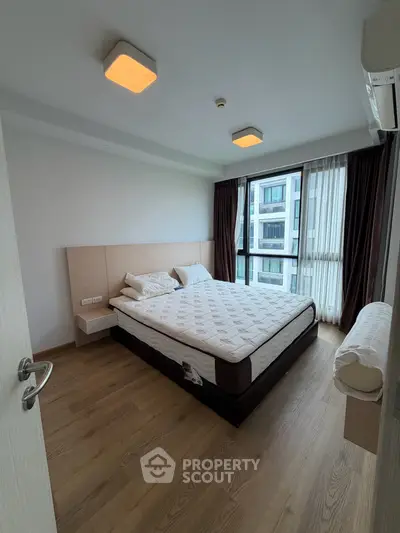 Modern bedroom with large window and wooden flooring in a stylish apartment.