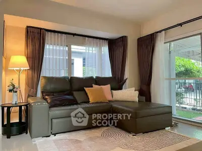 Stylish living room with modern leather sofa and large windows offering natural light and garden view.